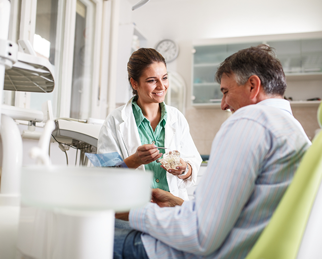 Smiling dentist showing a model of the teeth to a patient in the treatment chair