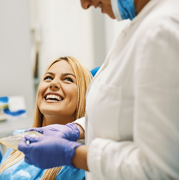 Woman in dental chair grinning up at her dentist