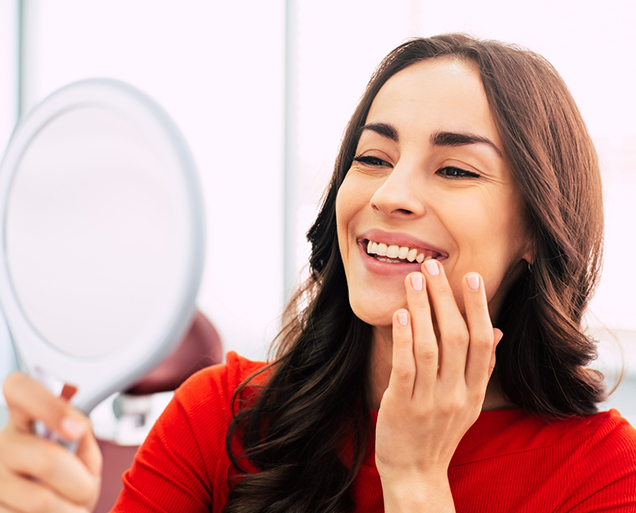 Woman admiring her smile in a mirror after cosmetic dentistry in Virginia Beach