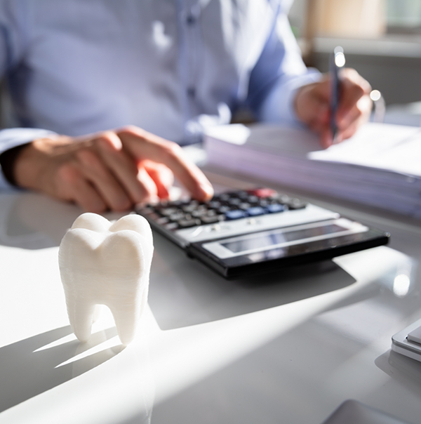 Person typing on calculator on desk next to model of fake tooth