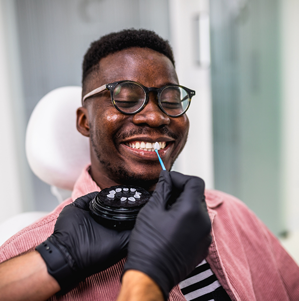 Man smiling while dentist holds a veneer next to his teeth