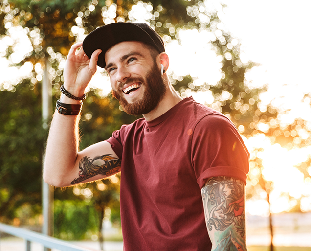 Young man with tattoos smiling outdoors after dental checkup and teeth cleaning