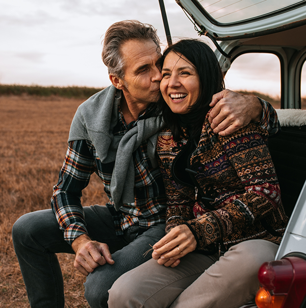 Man kissing woman on the side of her forehead while sitting in trunk of car