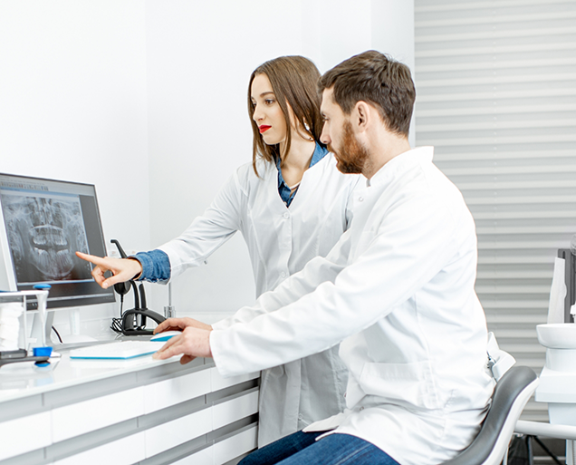 Two dentists looking at a computer screen showing x rays of teeth