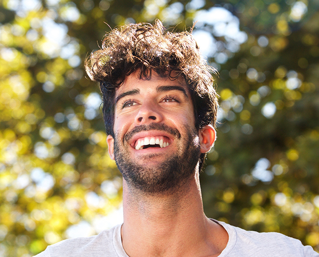 Man with curly dark hair grinning outdoors with veneers in Virginia Beach