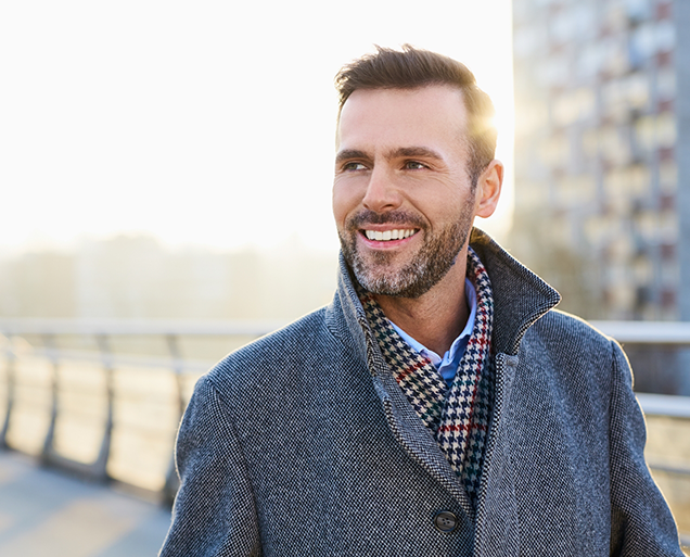 Man in coat and scarf smiling outdoors after gum disease treatment