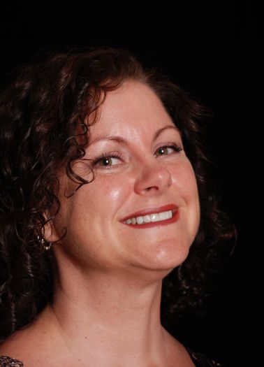 Woman with curly brown hair smiling against black background