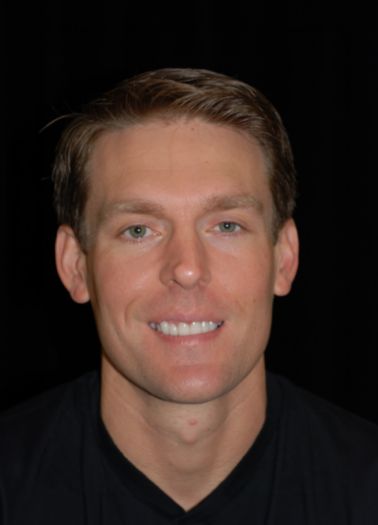 Man in black collared shirt smiling against black background