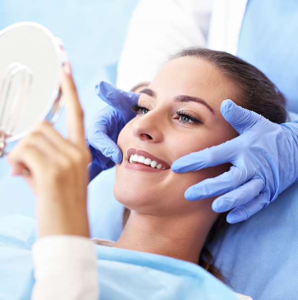 Woman in dental chair looking at her new smile in a mirror