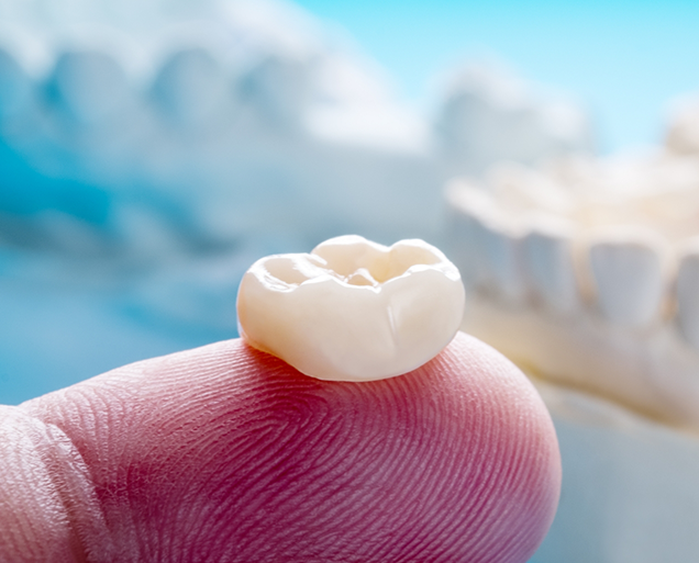 Close up of a porcelain dental crown resting on a finger