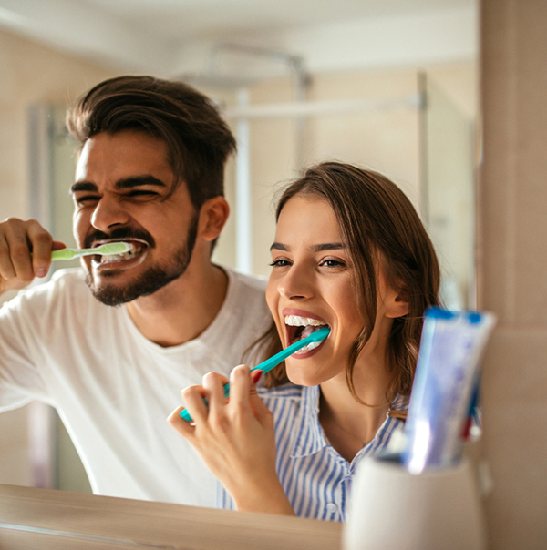 Young man and woman brushing their teeth together