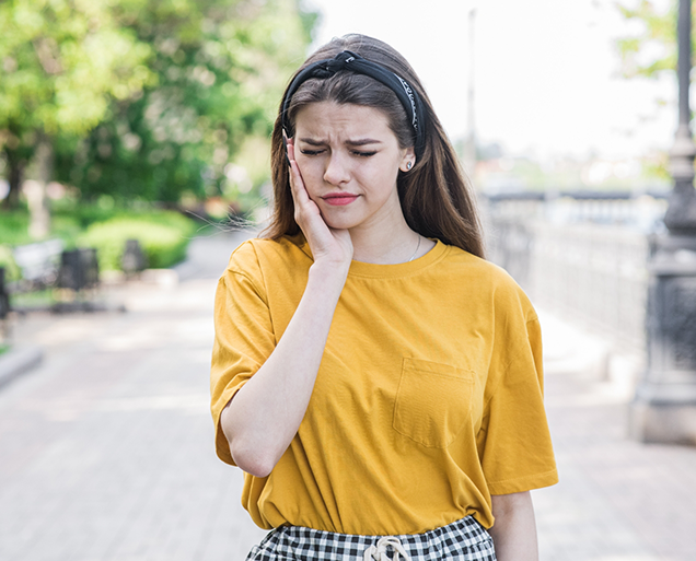 Young woman wincing and holding her cheek before root canal treatment in Virginia Beach