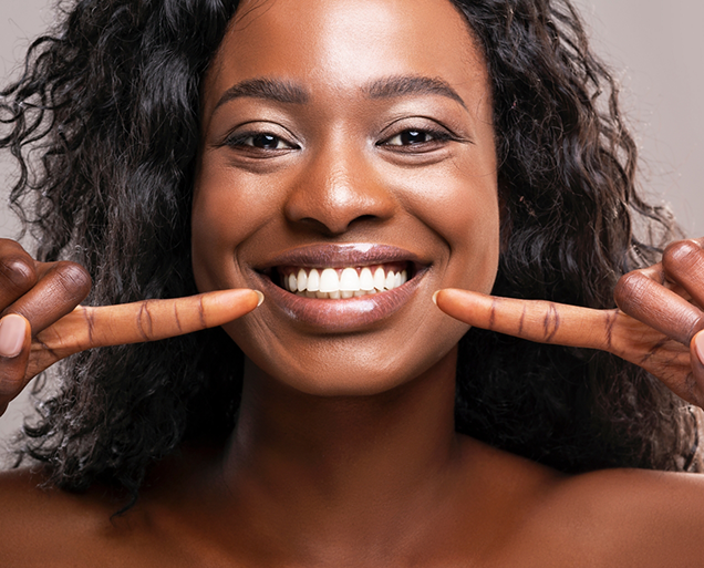 Woman pointing to her dazzling smile after teeth whitening in Virginia Beach