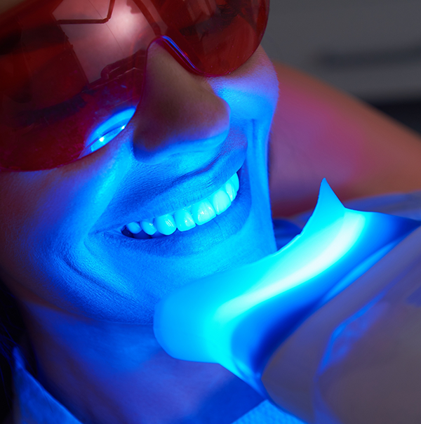 Dental patient having her teeth professionally whitened by a light