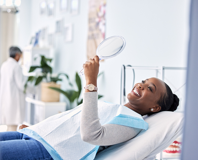 Woman in dental chair admiring her smile in a mirror