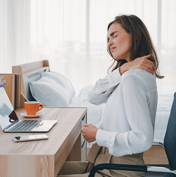 Woman sitting at desk and holding her shoulder blade while wincing in pain